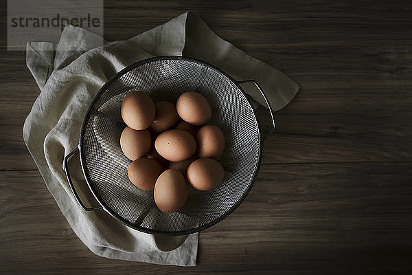 Draufsicht auf braune Eier in Sieb mit Serviette auf Holztisch