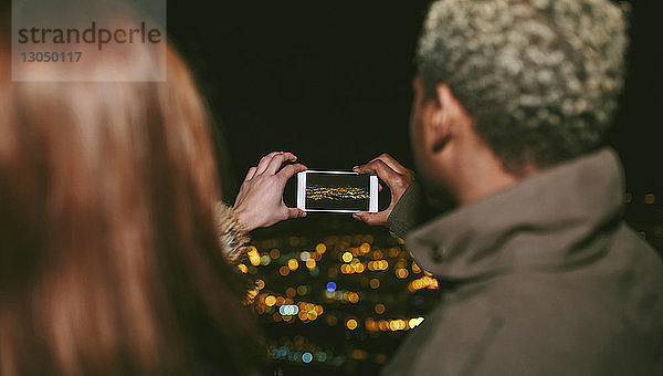 Rückansicht eines jungen Paares  das die Stadtlandschaft bei Nacht fotografiert