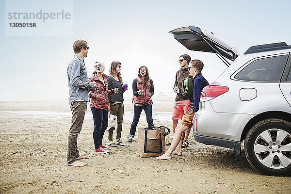 Glückliche Freunde stehen mit dem Auto am Strand