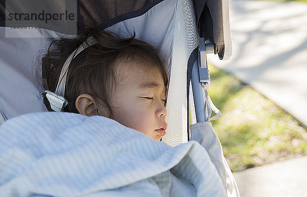 Nahaufnahme eines im Kinderwagen schlafenden Kleinkindes auf dem Rasen