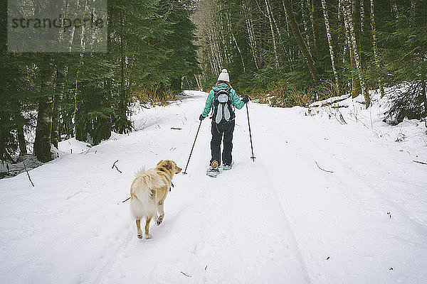 Rückansicht einer Frau mit Hund beim Skifahren auf schneebedecktem Feld