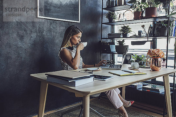 Geschäftsfrau  die Kaffee trinkt  während sie am Laptop im Heimbüro arbeitet