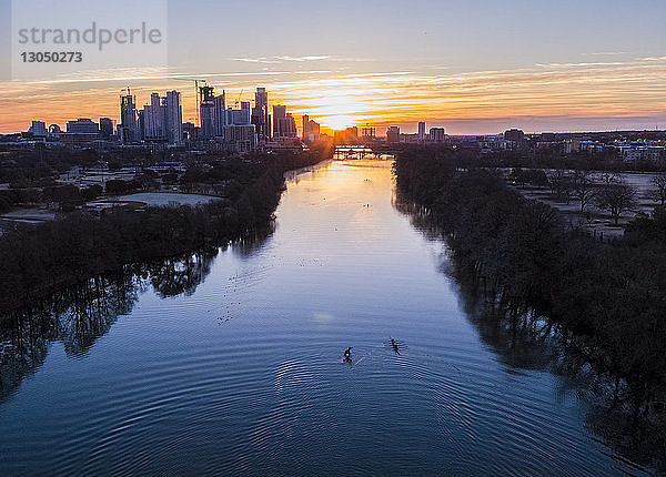 Hochwinkel-Distanzansicht von Menschen  die während des Sonnenaufgangs auf dem Lady Bird Lake gegen das Stadtbild segeln