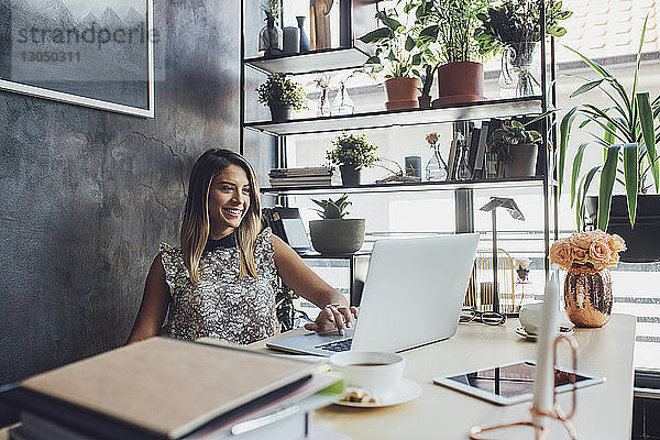 Lächelnde Geschäftsfrau arbeitet am Laptop im Heimbüro