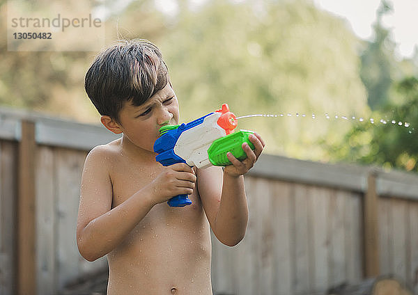 Junge  der mit einer Wasserpistole auf etwas zielt  während er im Hof steht