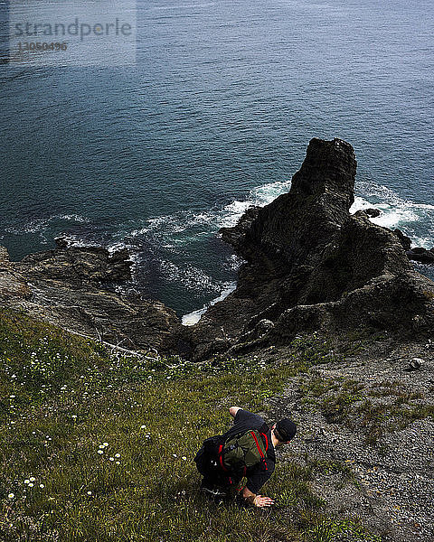 Hochwinkelaufnahme eines männlichen Wanderers auf einer Felsformation am Meer