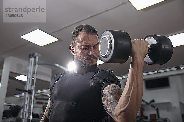 Selbstbewusster muskulöser Mann hebt Hantel im Fitnessstudio