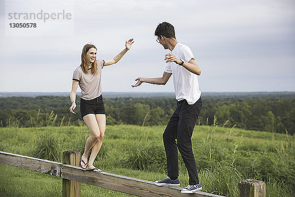 Glückliche Freunde spazieren auf Holzgeländer über grüne Landschaft gegen den Himmel