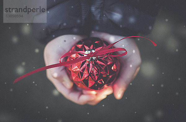 Abgetrennte Hände eines Jungen  der während des Schneefalls ein Weihnachtsornament hält