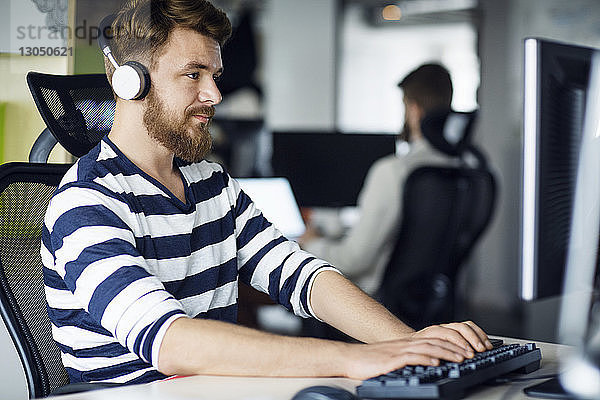 Geschäftsmann  der Musik hört  während er im Kreativbüro einen Computer benutzt