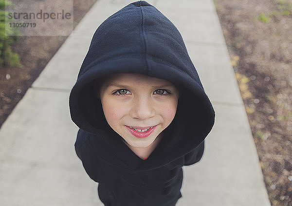 Hochwinkelporträt eines glücklichen Jungen mit schwarzer Kapuzenjacke  der auf einem Fußweg steht