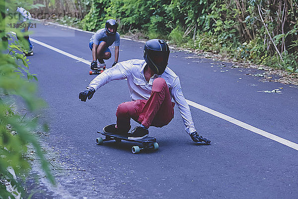 Männliche Freunde kauern beim Skateboardfahren auf der Straße