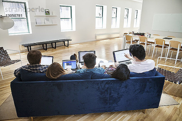 Rückansicht von Geschäftsleuten  die Laptops auf dem Sofa im Kreativbüro benutzen