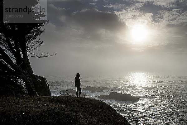 Silhouette eines Teenagers  der den Blick vom Meer gegen den Himmel richtet