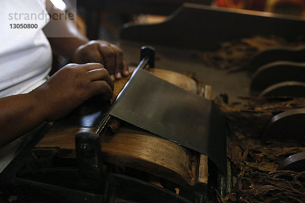 Geschnittene Hände eines Mannes bei der Herstellung einer Zigarre mit Tabakblättern in einem Workshop
