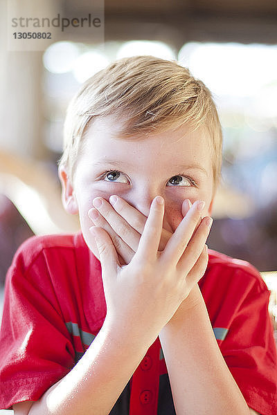 Nahaufnahme eines Jungen  der aufschaut  während er zu Hause den Mund bedeckt