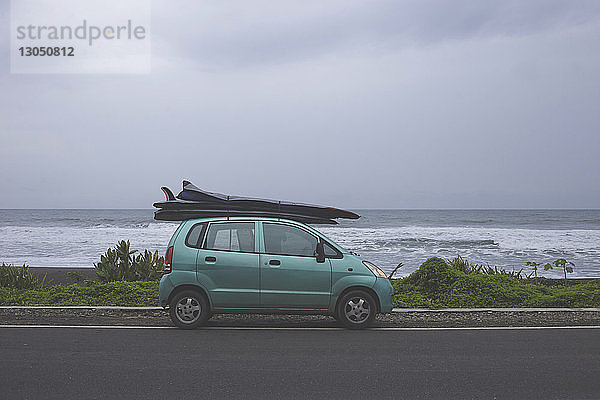 Surfbretter auf dem Autodach auf der Straße am Meer vor bewölktem Himmel geparkt