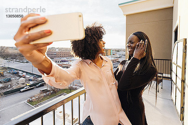 Geschäftsfrau hält Smartphone in der Hand  während sie eine Kollegin auf dem Hotelbalkon anschaut