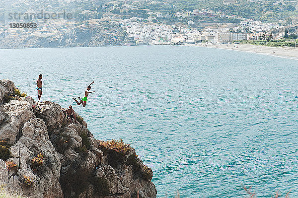 Freunde betrachten Mann  der von einer Klippe ins Meer springt