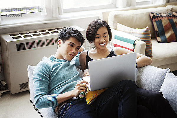 Glückliches junges Paar benutzt Laptop  während es zu Hause auf dem Sofa liegt
