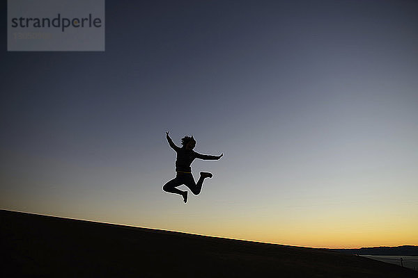 Silhouettenfrau springt in der Dämmerung an Land gegen den klaren Himmel