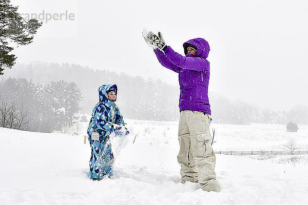 Mutter und Tochter spielen mit Schnee  während sie auf dem Feld gegen den Himmel stehen
