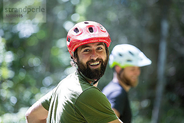 Porträt eines glücklichen Wanderers mit Fahrradhelm und Freund im Hintergrund