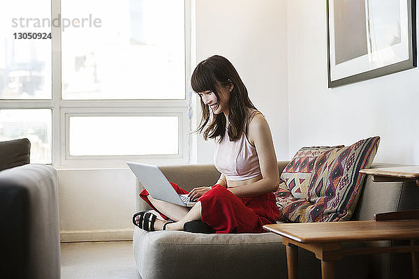Lächelnde Frau benutzt Laptop  während sie im Büro auf dem Sofa sitzt