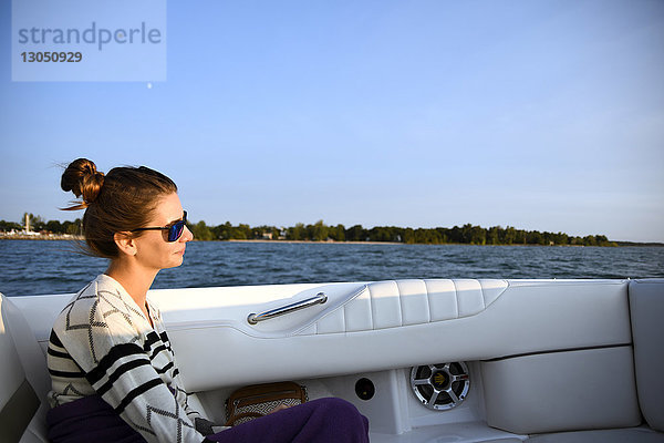 Seitenansicht einer Frau  die eine Sonnenbrille trägt  während sie in einem Boot auf dem See vor strahlend blauem Himmel sitzt