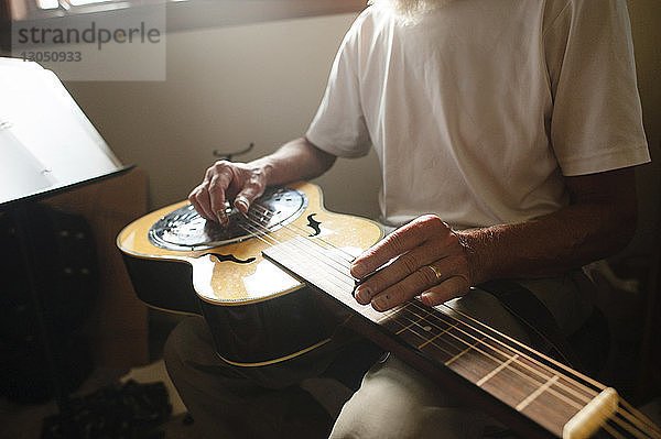 Mittelteil eines älteren Mannes  der zu Hause Gitarre lernt