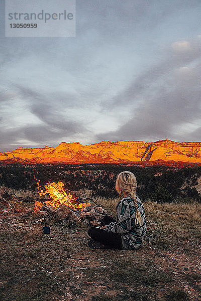 Frau sitzt am Lagerfeuer gegen Berge