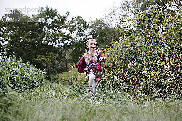 Fröhliches Mädchen läuft in voller Länge auf dem Spielfeld im Park