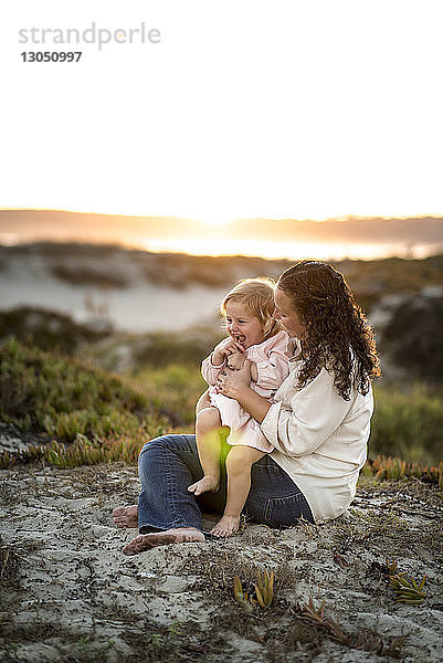 Mutter und Tochter sitzen auf Sand gegen den Himmel