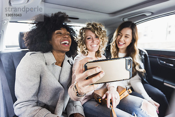 Fröhliche Geschäftsfrauen  die im Auto sitzen und sich mit einem Smartphone selbstständig machen