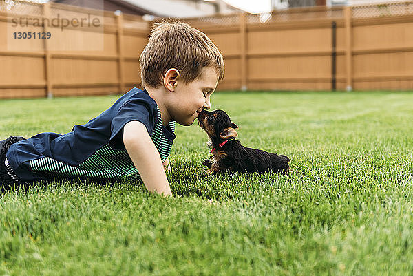 Junge küsst Hund  während er auf Grasfeld liegt