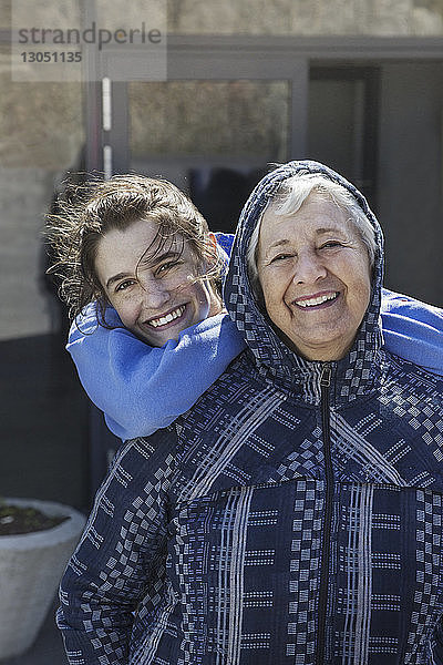 Porträt einer glücklichen Grossmutter mit Enkelin  die im Winter vor dem Haus steht