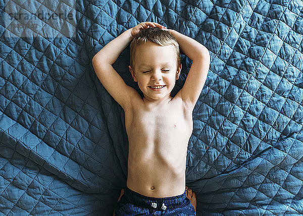Draufsicht eines glücklichen Jungen mit geschlossenen Augen auf dem Bett liegend