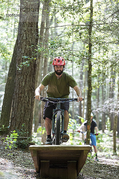 Wanderer macht Stunt beim Mountainbikefahren mit Freund im Hintergrund im Wald