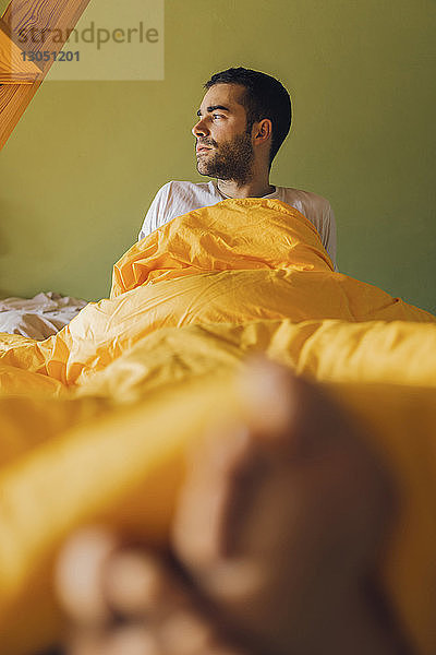 Nachdenklicher Mann schaut weg  während er sich zu Hause im Bett entspannt