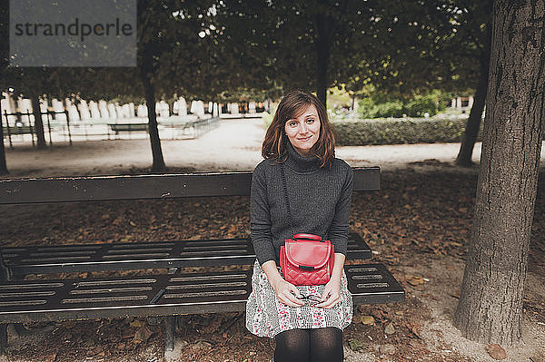 Porträt einer lächelnden Frau mit Geldbörse auf einer Parkbank sitzend