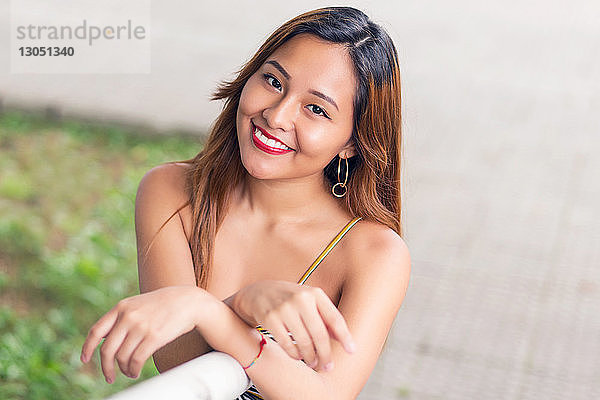 Hochwinkelporträt einer lächelnden jungen Frau  die am Geländer eines Parks steht