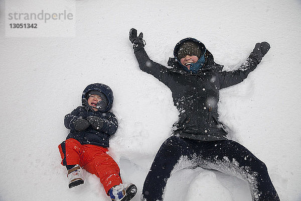 Hochwinkelaufnahme der Mutter  die lacht  während der Sohn bei Schneefall auf schneebedecktem Land weint