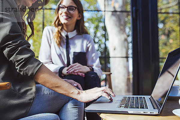 Mittelsektion einer Frau  die einen Laptop-Computer benutzt  während sie mit einem Kollegen im Café sitzt