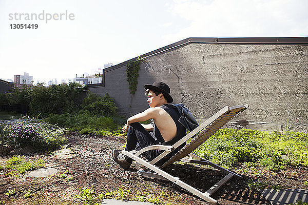 Seitenansicht eines nachdenklichen Mannes  der auf einem Liegestuhl auf der Terrasse sitzt