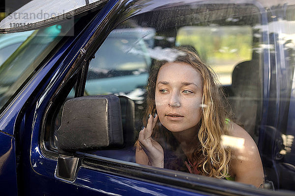 Frau berührt beim Blick in den Seitenspiegel eines Autos die Wange