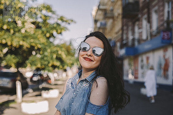 Lächelnde junge Frau mit Sonnenbrille  die in der Stadt steht