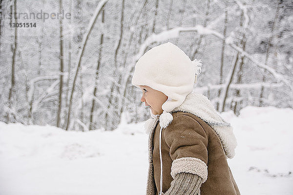 Seitenansicht eines Mädchens in warmer Kleidung beim Wegschauen auf ein verschneites Feld