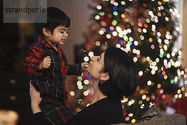 Seitenansicht der Mutter mit Sohn bei beleuchtetem Weihnachtsbaum zu Hause