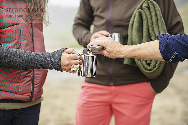 Ausgeschnittenes Bild eines Mannes  der am Strand Alkohol in den Becher einer Frau gießt