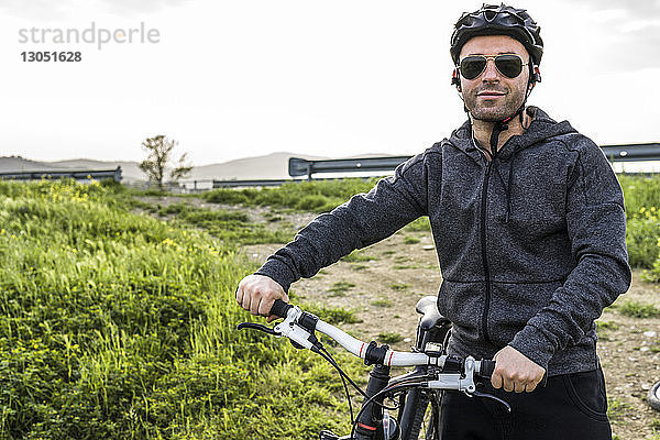 Bildnis eines Mannes mit Fahrrad auf einem Feld vor klarem Himmel stehend